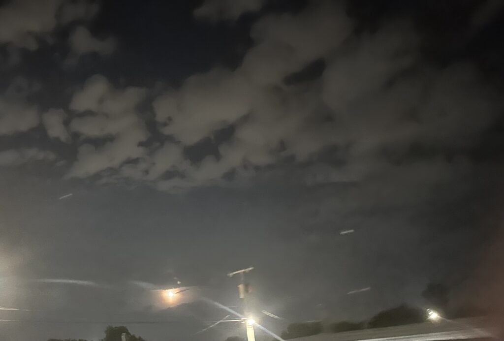 The moon near a light pole, with broken clouds above in the night sky.